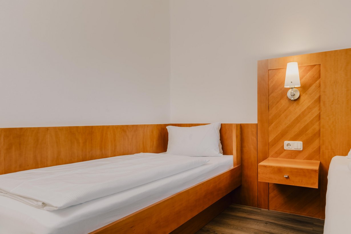 Ein komfortables Einzelbett steht vor einer halb mit Holz getäfelten Wand. Recht daneben sieht man die Kante eines weiteren Bettes.